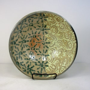 May include: A large ceramic bowl with a green and yellow glaze. The bowl features a unique design with a pattern of circles and lines.