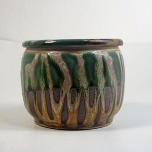 Op de afbeelding: Een keramische plantenpot met een groene, bruine en roze glazuur. De pot heeft een ronde vorm en een brede rand.