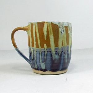 May include: A ceramic mug with a brown, yellow, and blue glaze. The mug has a wide, rounded body and a handle.