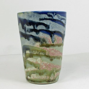 May include: A ceramic cup with a blue, green, and pink glaze. The glaze has a streaky, abstract pattern.