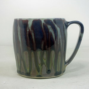 May include: A ceramic mug with a unique glaze pattern in shades of brown, purple, and green. The mug has a rounded body and a handle.