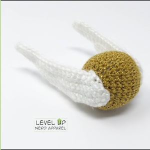May include: A crocheted golden snitch with white wings. The snitch is a popular object from the Harry Potter series.
