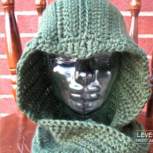 May include: A green crocheted hooded hat and matching scarf. The hat has a wide brim and the scarf is long and thin. The hat and scarf are both made with a simple stitch pattern.