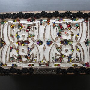 May include: A wooden box with a black trim and a white carved design. The box is covered in colourful beads and has the word "kindness" written on the front.