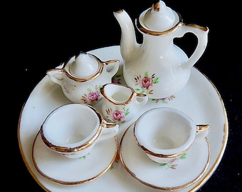 May include: A white porcelain tea set with floral designs. The set includes a teapot, creamer, sugar bowl, and two teacups and saucers.