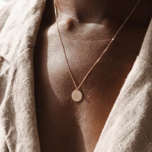 May include: A gold chain necklace with a round pendant featuring the letter "S" engraved on it.