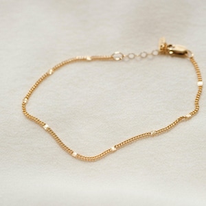 May include: Delicate gold-colored bracelet with a chain-link design. The bracelet features small, sparkling accents evenly spaced along the chain. The clasp and adjustable chain are also gold-toned, creating a cohesive and elegant piece of jewelry.