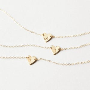 May include: Three gold necklaces with heart pendants, each bearing a single initial: "A", "M", and "K". The necklaces are displayed against a white backdrop, showcasing the delicate chain and heart design.