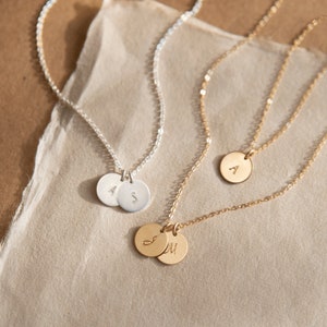 May include: Two delicate necklaces with initial charms. One necklace is silver with two charms, one with the letter 'A' and the other with the letter 'S'. The other necklace is gold with two charms, one with the letter 'J' and the other with the letter 'M'.