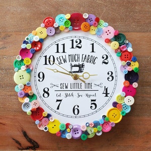 May include: A white clock with black numbers and hands, surrounded by colorful buttons. The clock face reads "Sew Much Fabric" and "Sew Little Time".