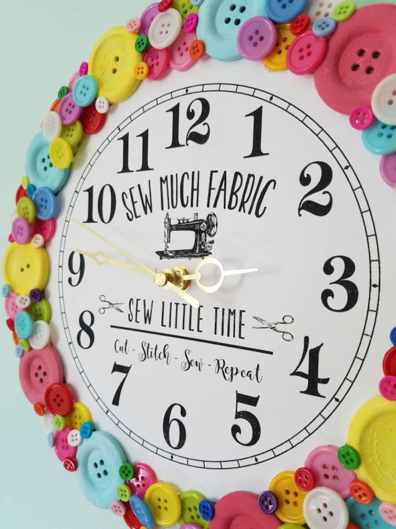 May include: A white clock with black numbers and hands, surrounded by colorful buttons. The clock face reads "10 Sew Much Fabric" and "Sew Little Time Cut - Stitch - Sew - Repeat".