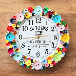 May include: A white clock with black numbers and hands, surrounded by colorful buttons. The clock face reads "Sew Much Fabric" and "Sew Little Time".
