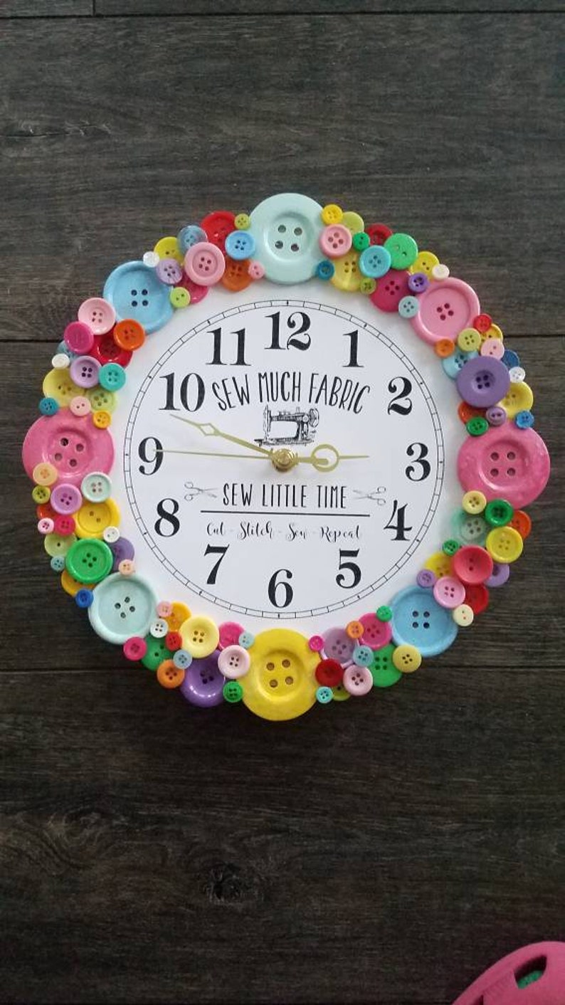 May include: A white clock with black numbers and a sewing machine design. The clock is surrounded by colorful buttons. The text on the clock reads "10 Sew Much Fabric" and "Sew Little Time Cut Stitch Sew Repeat".