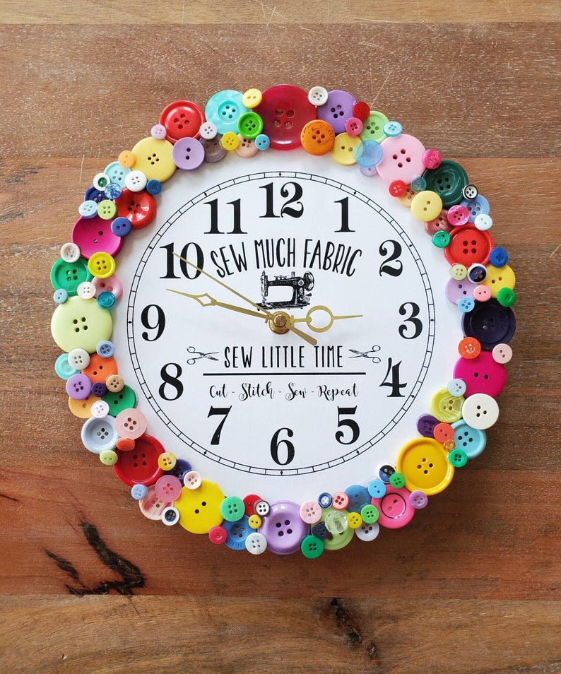 May include: A white clock with black numbers and hands, surrounded by colorful buttons. The clock face reads "Sew Much Fabric" and "Sew Little Time".