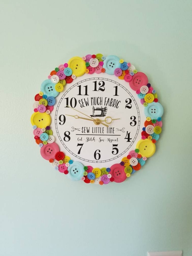 May include: A white clock with black numbers and a sewing machine graphic. The clock is surrounded by a ring of colorful buttons.