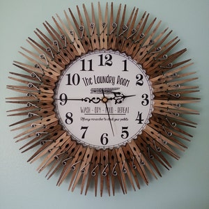 May include: A clock made from wooden clothespins with a white face that says "The Laundry Room" and "Wash - Dry - Fold - Repeat" with a reminder to check your pockets. The clock hands are black and gold.