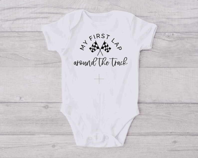 May include: White baby onesie with black text that reads "My First Lap Around The Track" with a checkered flag graphic.