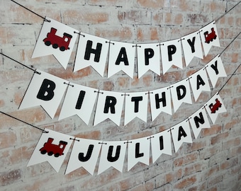 May include: White banner with black letters spelling "Happy Birthday Julian" with red toy train cutouts on each end.