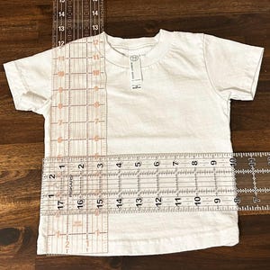 May include: White t-shirt with a ruler measuring the length and width. The ruler shows measurements in inches.