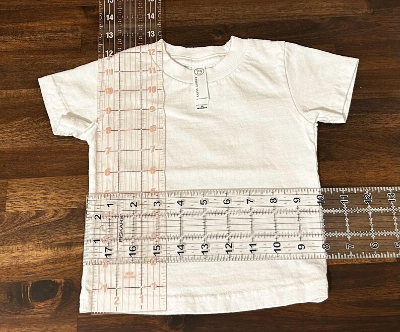 May include: White t-shirt with a ruler measuring the length and width. The ruler shows measurements in inches.