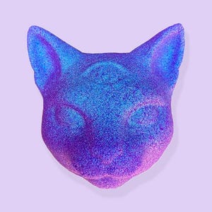 May include: A cat-shaped object with a shimmering, iridescent finish. The color transitions from blue to purple, creating a gradient effect. The cat's face is detailed with eyes and ears, set against a light purple background.
