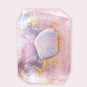 May include: A clear, pink and purple soap bar with gold flecks and a pink and purple stone embedded in the center.