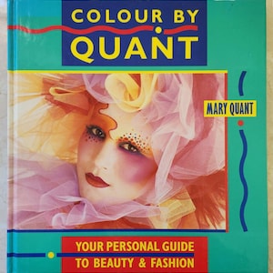 Op de afbeelding: Een boek getiteld "Colour by Quant" van Mary Quant. De omslag toont een vrouw met kleurrijke make-up en een roze en gele hoed. De tekst "Your Personal Guide to Beauty & Fashion" staat onderaan de omslag.