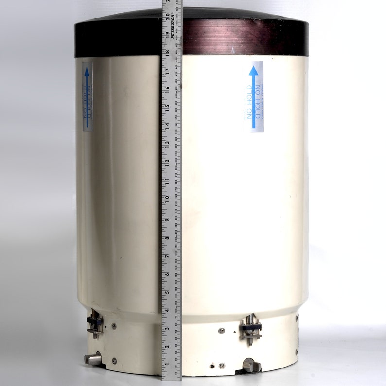 Puede incluir: Un instrumento meteorol&oacute;gico cil&iacute;ndrico blanco con una parte superior negra y una banda marr&oacute;n. El instrumento tiene una regla junto a &eacute;l para la escala. El instrumento tiene una pegatina azul con el texto "NO HOLD ON TOP" y una flecha apuntando hacia arriba.