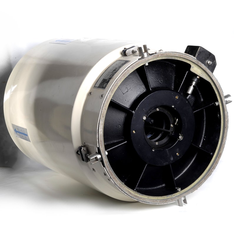 Puede incluir: Un objetivo de c&aacute;mara cil&iacute;ndrico blanco con un anillo de metal negro y una palanca plateada. El objetivo tiene una tapa de metal negro con una serie de agujeros alrededor del borde.