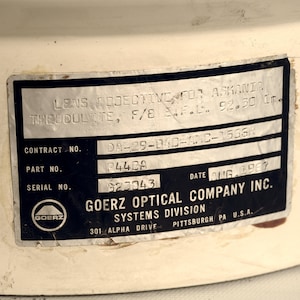 Puede incluir: Una etiqueta en blanco y negro con el texto "GOERZ OPTICAL COMPANY INC. SYSTEMS DIVISION 301 ALPHA DRIVE PITTSBURGH PA U.S.A." y el texto "LENS OBJECTIVE FOR ASKANIA THEODOLITE, F/8 E.F.L. 92.30 In DA-29-040-AMC-15664 CONTRACT NO. P442A PART NO. 623043 SERIAL NO. DATE AUG 1960". La etiqueta tiene un logotipo en blanco y negro de un c&iacute;rculo con la palabra "GOERZ" dentro.