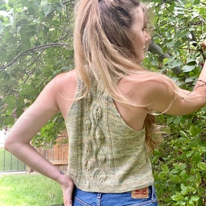 May include: A green and yellow knitted tank top with a leafy pattern. The tank top is sleeveless and has a scoop neck.