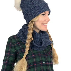 May include: A blue knitted beanie with a white pom pom and a matching blue knitted infinity scarf.