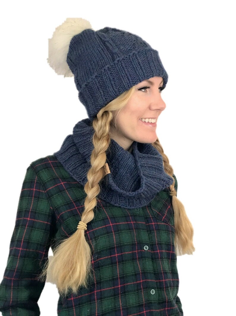 May include: A blue knitted beanie with a white pom pom and a matching blue knitted infinity scarf.