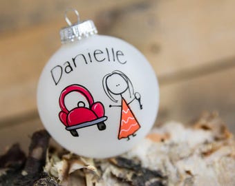 May include: White Christmas bauble with a red car and a stick figure woman holding a key. The bauble is personalised with the name "Danielle".