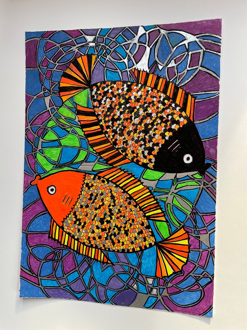 Op de afbeelding: Kunstafdruk met kleurrijke vissen. Twee vissen met oranje, zwarte en gele schubben tegen een achtergrond in glas-in-loodstijl van blauw, paars en groen. Het kunstwerk is omlijnd met zilver.