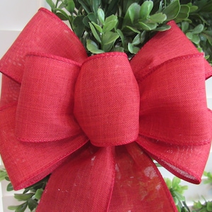 May include: A large, red, burlap bow with a center loop. The bow is tied around a green wreath.