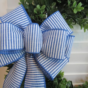 May include: A blue and white striped bow with a white background and blue stripes. The bow is made of fabric and has a stitched edge.