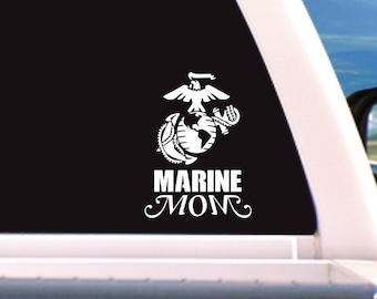May include: White vinyl decal with the Marine Corps emblem and the text "Marine Mom" on a black background. The decal is on the back window of a white pickup truck.