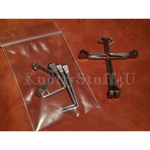 May include: Four silver horseshoe nails in a clear plastic bag next to a silver horseshoe nail cross.