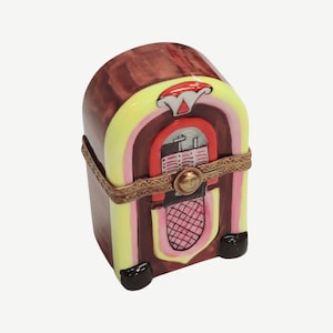 May include: A ceramic figurine of a vintage jukebox with a brown, yellow, pink, and red color scheme. The jukebox has a record selection panel and a speaker grill.