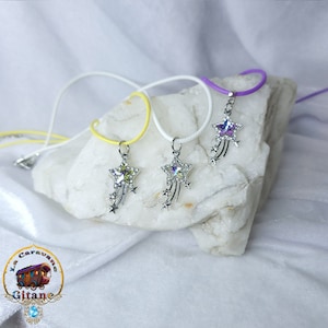 Peut inclure: Trois colliers avec des pendentifs en forme d'étoile filante. Les pendentifs sont en argent avec une étoile en cristal transparent et de plus petites étoiles en argent qui traînent derrière. Les colliers sont sur une surface blanche et sont disponibles en jaune, blanc et violet.