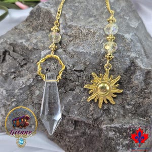 May include: A gold-toned chain features two dangling charms: a clear, faceted, pointed crystal pendant suspended from a twisted gold ring, and a gold sun-shaped charm. Both charms are accented with small, clear, iridescent glass beads.