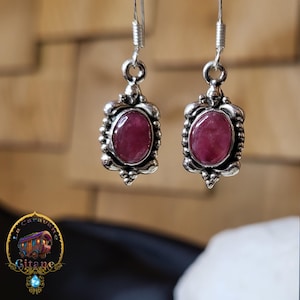 Może przedstawiać: Para srebrnych kolczyków z różowymi, owalnymi kamieniami szlachetnymi osadzonymi w ozdobnych srebrnych oprawach.