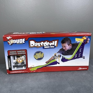 May include: A boxed Daredevil race set featuring a purple and green track with a ramp. The box has the words "Daredevil race set" and "Over 3 feet" printed on it. A Barney figure on a skateboard is also included.