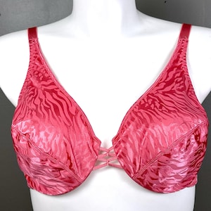 May include: A bright pink bra featuring a tonal zebra stripe pattern throughout the fabric. The garment includes adjustable shoulder straps, a deep V-neckline, and a central bridge detail with three thin, crisscrossing horizontal fabric bands.