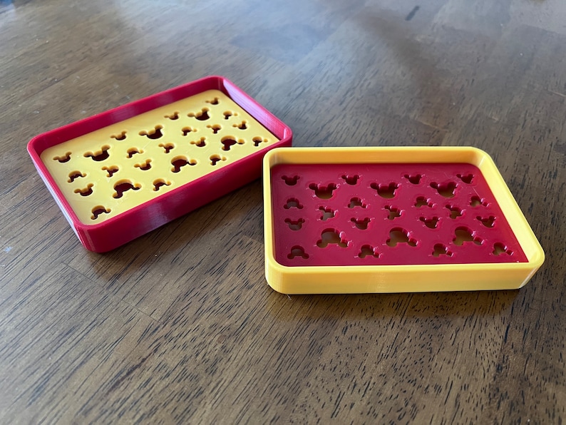 May include: Two yellow and red soap dishes with Mickey Mouse head cutouts. The dishes are made of plastic and are designed to hold soap bars.