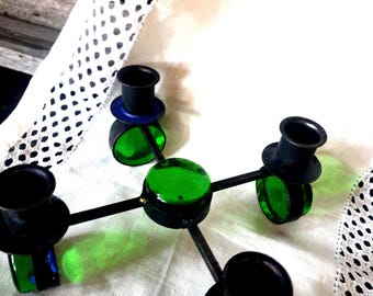 May include: A unique, multi-arm candle holder with a central green glass orb and four black candle cups. Each cup sits atop a green glass base with a blue accent. The metal arms extend from the center, creating a modern design.