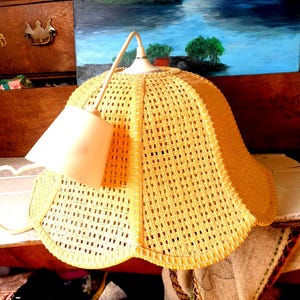 May include: A yellow wicker pendant light fixture with a white shade. The light fixture is hanging from a white cord.