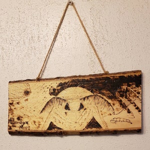 May include: A wood burned art piece with a detailed image of a moth. The piece is hanging from a string and has the signature "Bombyx Mori" in the bottom left corner.