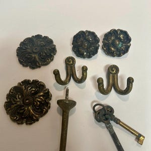 May include: Assortment of antique brass hardware, including two ornate rosettes, two double hooks, a decorative finial, and two skeleton keys.